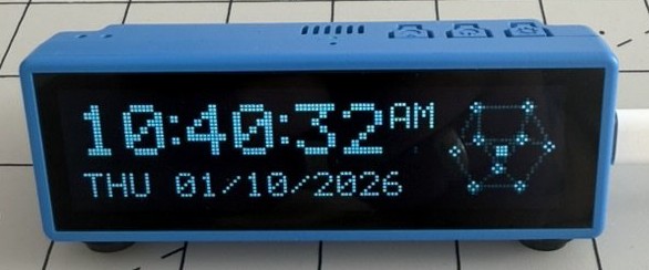 Tick, Pan's blue alarm clock, showing 10:40:32 AM and THU 01/10/2026 in blue dot-matrix type, with the cube face drawn in nodes beside the time